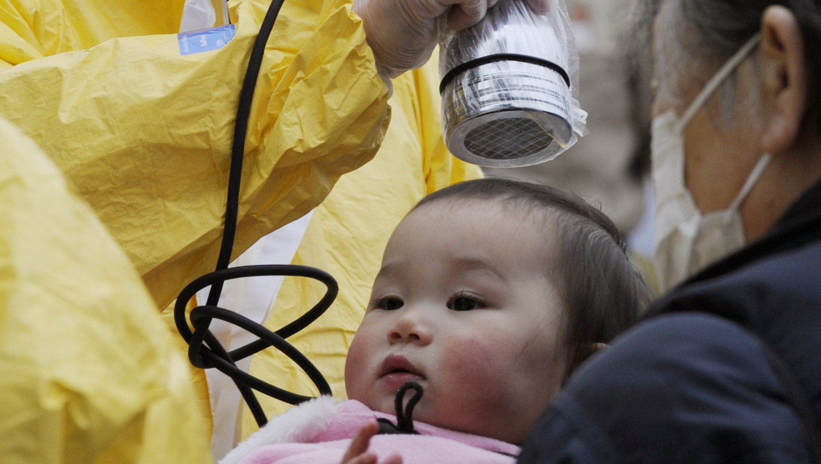 Japonský záchranár meria úroveň ožiarenia u dieťaťa pomocou dozimetru